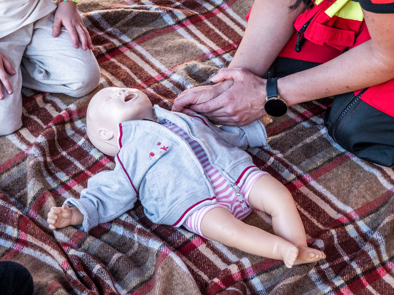 Paramedic performing CPR on baby mannequin during outdoor training session.